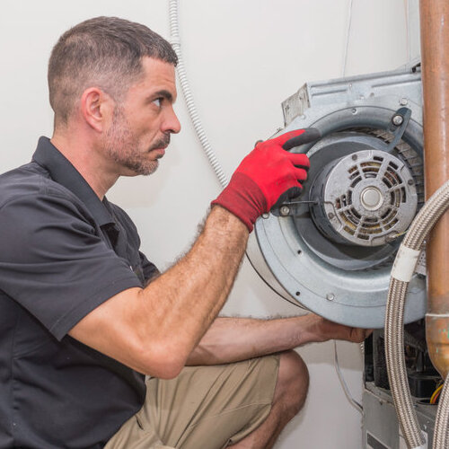 HVAC technician removing a furnace blower motor from a commercial heat pump. Repair man wearing a uniform and safety gloves.
