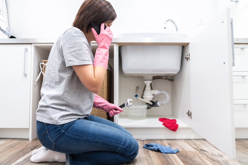 Woman sitting near leaking sink calling for help