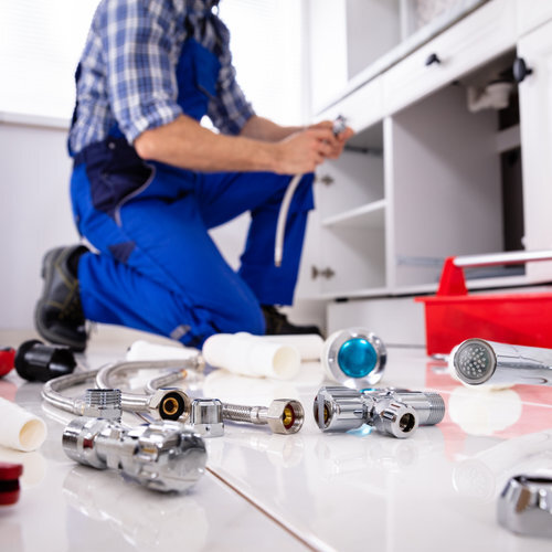 Plumber Tools And Equipment On Floor In Kitchen With Plumber Installing The Sink At Background