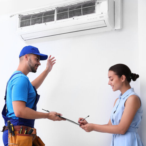 Professional technician speaking with woman about air conditioner indoors