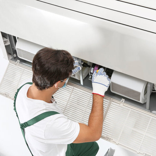 Young male technician repairing air conditioner indoors